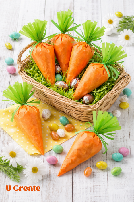 DIY Easter carrot treat bags made with orange tissue paper and candy eggs displayed in a wicker Easter basket