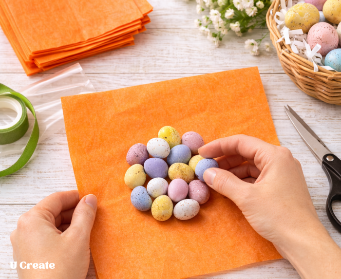 Adding candy eggs to tissue paper to make Easter carrot treat bags